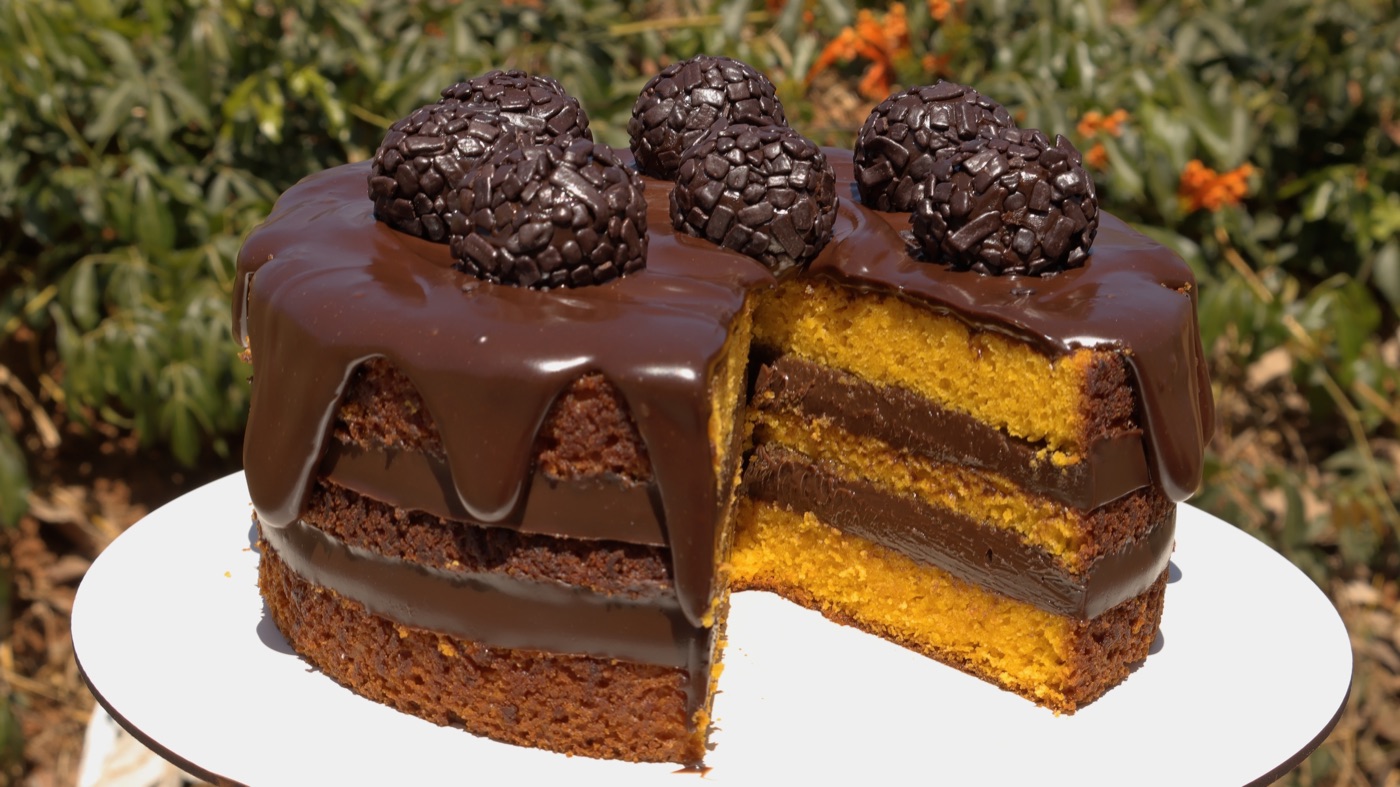 Bolo de cenoura coberto de ganache com brigadeiros, cortado mostrando as camadas retas