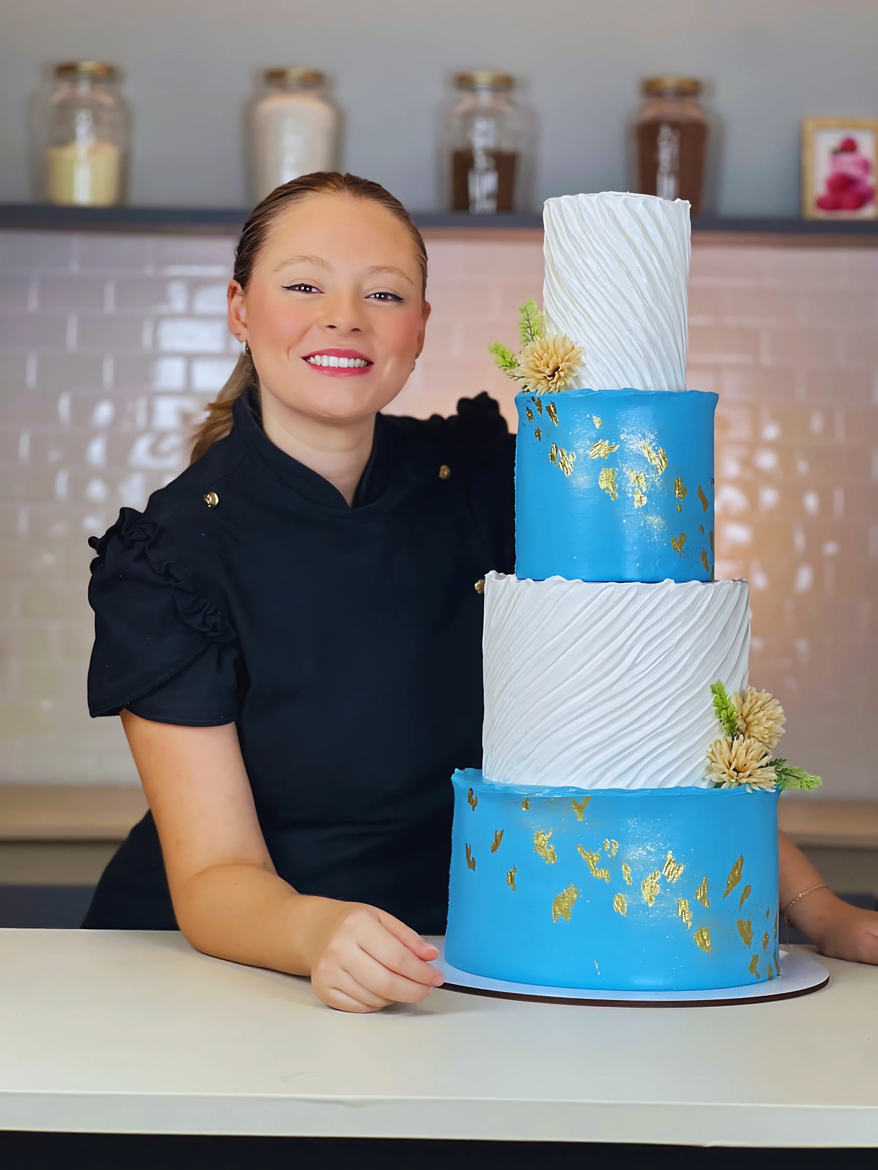 Chef Beatriz Ramalho ao lado de um bolo de andar azul com detalhes dourados